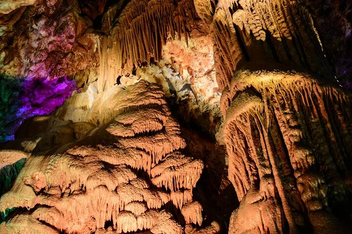 Large, intricately shaped stalactites and stalagmites inside the illuminated Venetsa Cave.