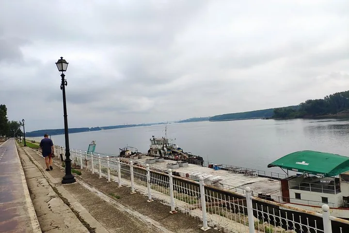 Person walking along a river promenade with boats docked nearby.